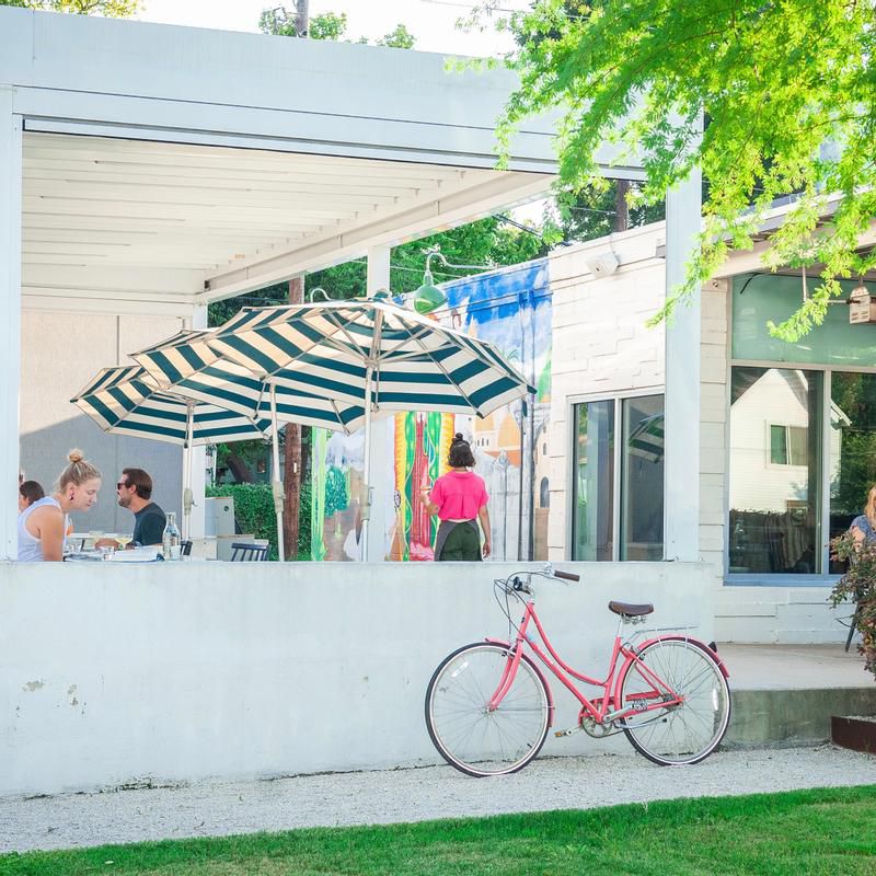 Diners sit outside on a patio that’s painted white with green and white striped umbrellas.