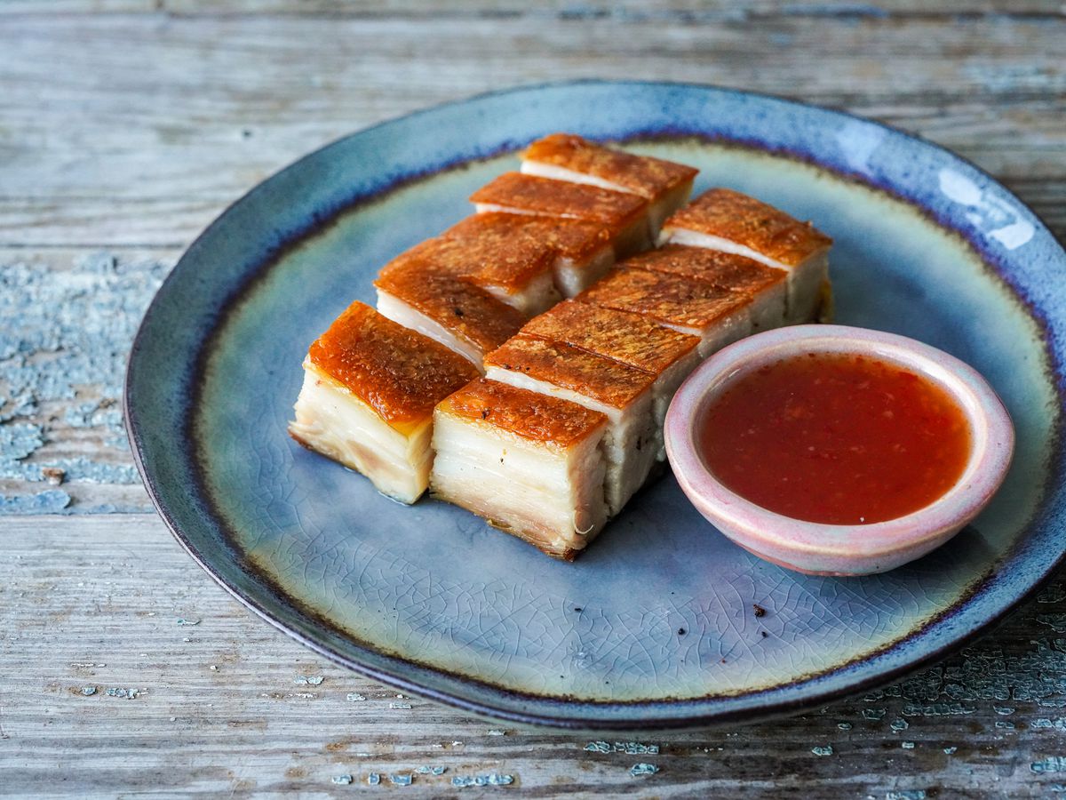 Cut pieces of fried pork belly on a plate with a condiment saucer of red ketchup.