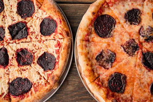 Two pies with burnt pepperoni slices on top sit side by side on silver trays.
