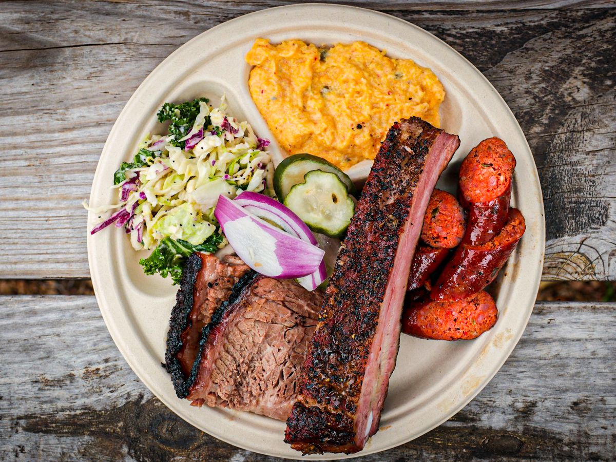 A barbecue plate filled with ribs, brisket, potato salad, and slaw.