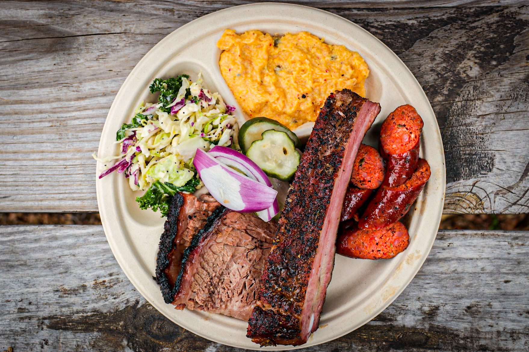 A barbecue plate filled with ribs, brisket, potato salad, and slaw.
