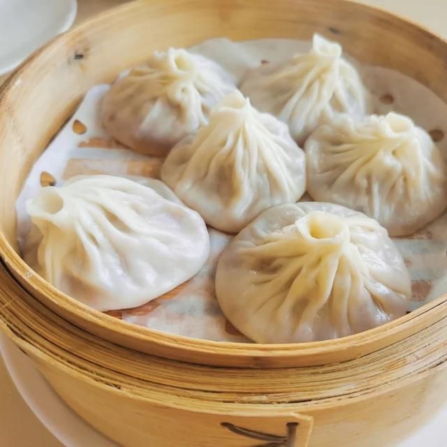 A wooden basket holds a half dozen steamed dumplings.