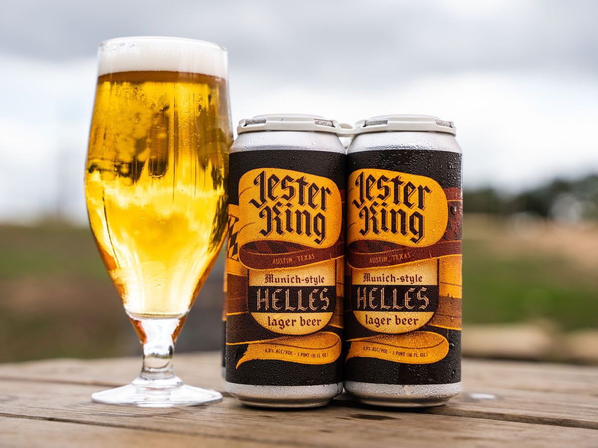 A tall glass of beer next to two cans of beer.