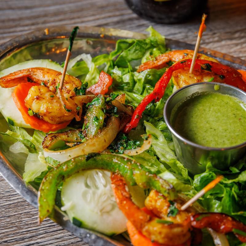 A plate of shrimp and vegetables with a dipper of salsa verde.