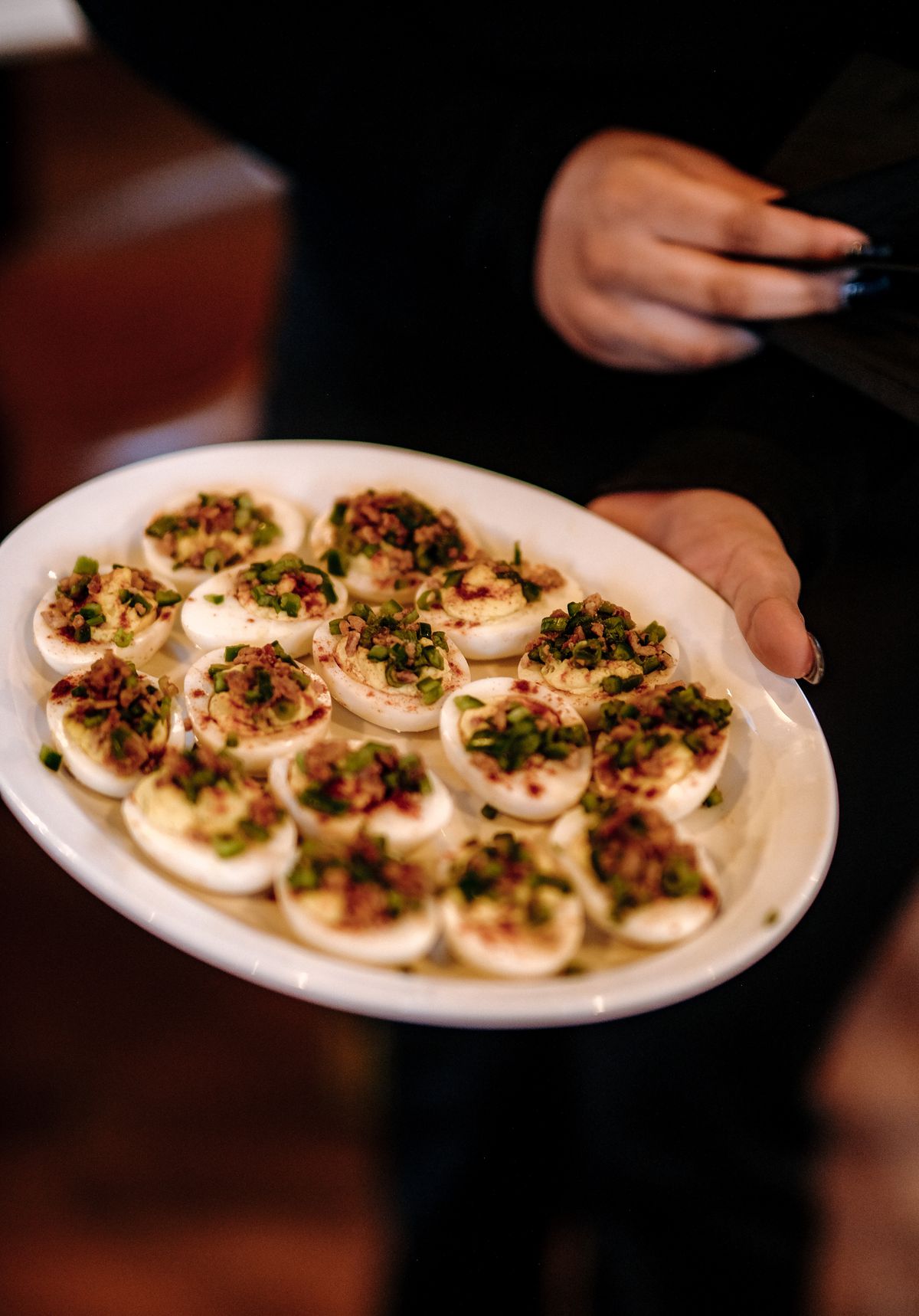 A person holds a plate loaded with deviled eggs towards the camera.