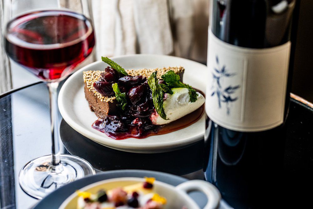 A plate with a berry pie and ice cream sits on a black table. Next to it are a bottle and glass of wine.