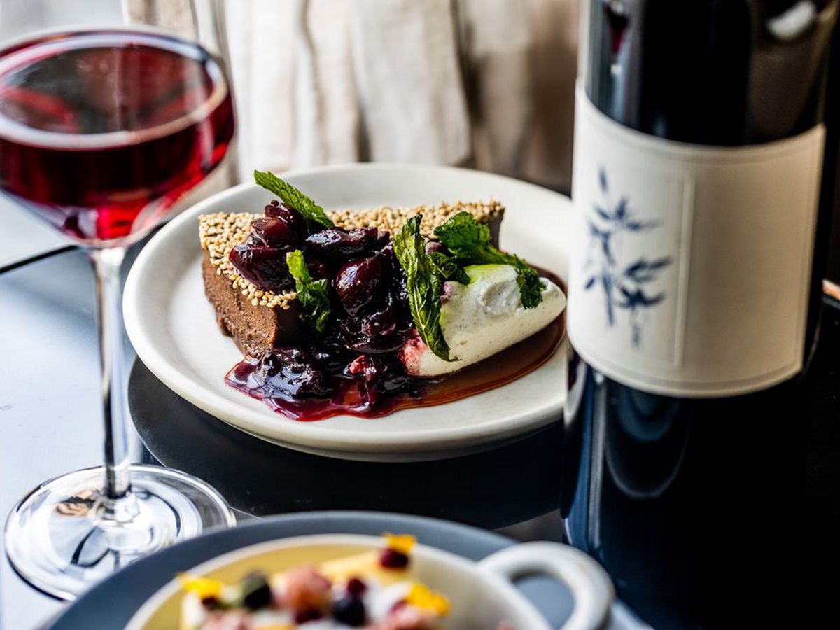 A plate with a berry pie and ice cream sits on a black table. Next to it are a bottle and glass of wine.