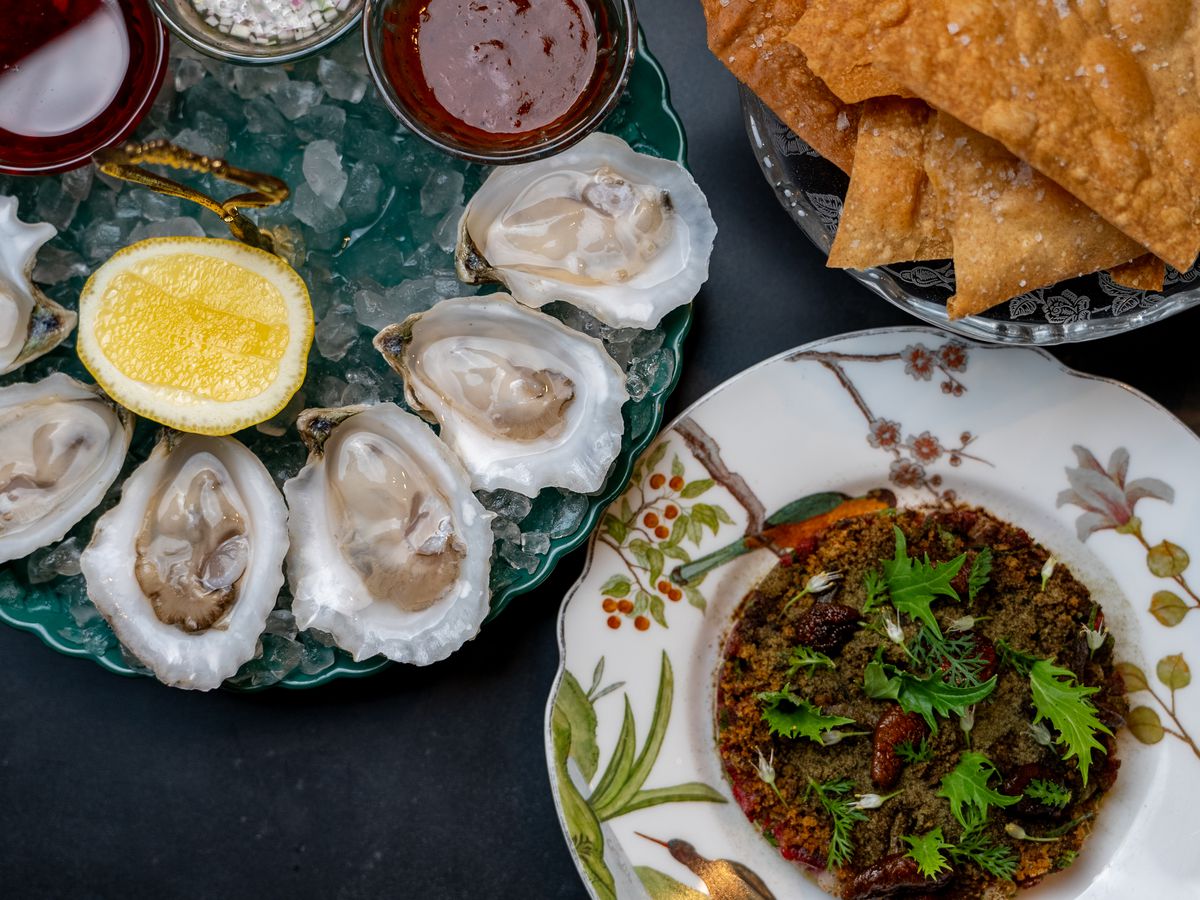 A plate with oysters on the half shell and sauces sits on the left. To the right is a plate with carpaccio. Above it is a plate with crisp breads.