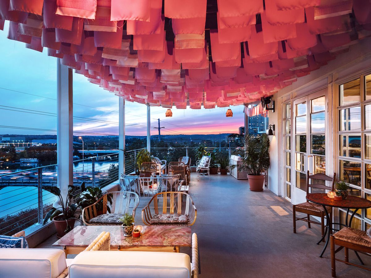 An outdoor patio looks over Texas Hill Country at sunset, with red flags hanging from the roof.