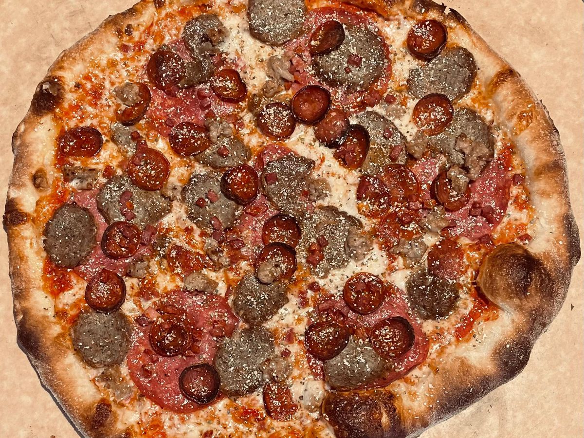 A pizza topped with pepperoni, sausage, and other meats sits on a table.