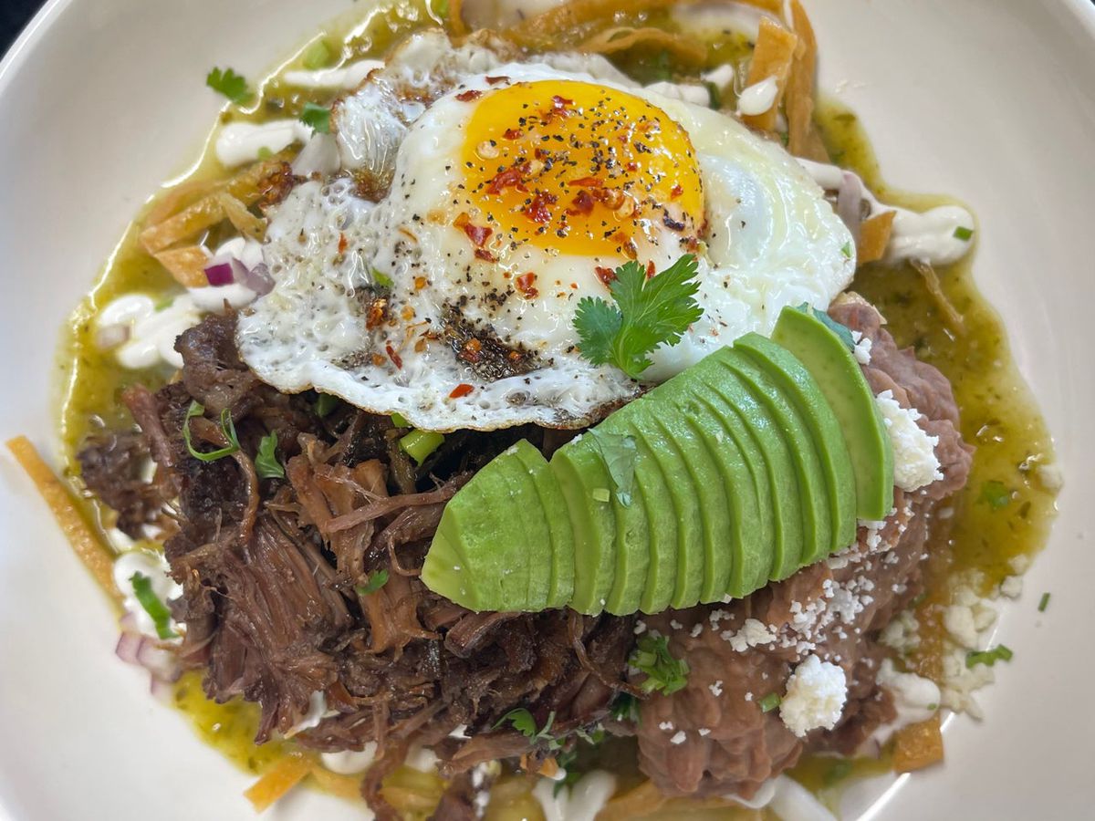 A plate of shredded meat, an egg, broth, and sliced avocados.