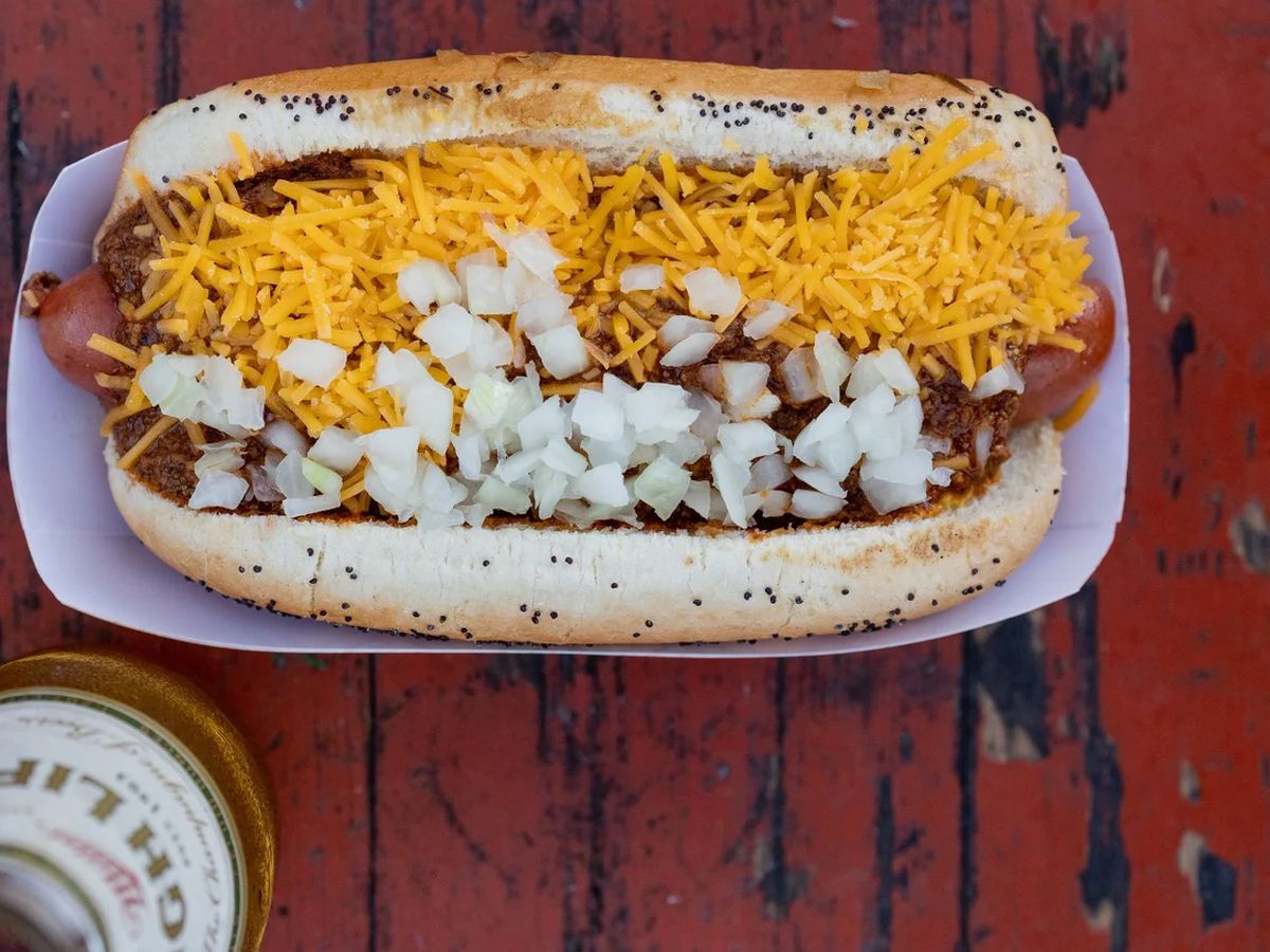 A hot dog with shredded yellow cheese and diced onions.