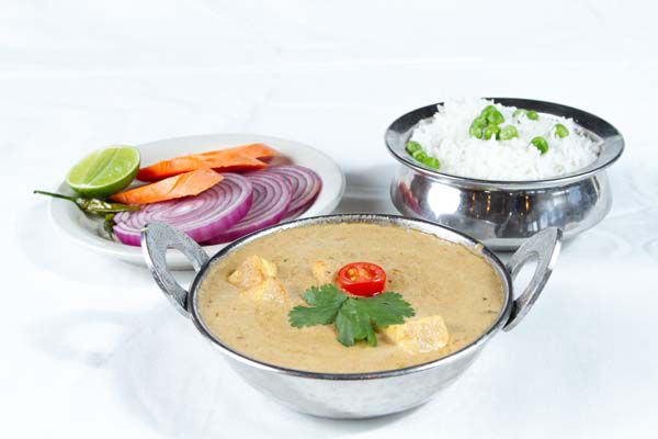 Two silver bowls hold a soup, rice, and a third ceramic bowl holds onions and a lime.