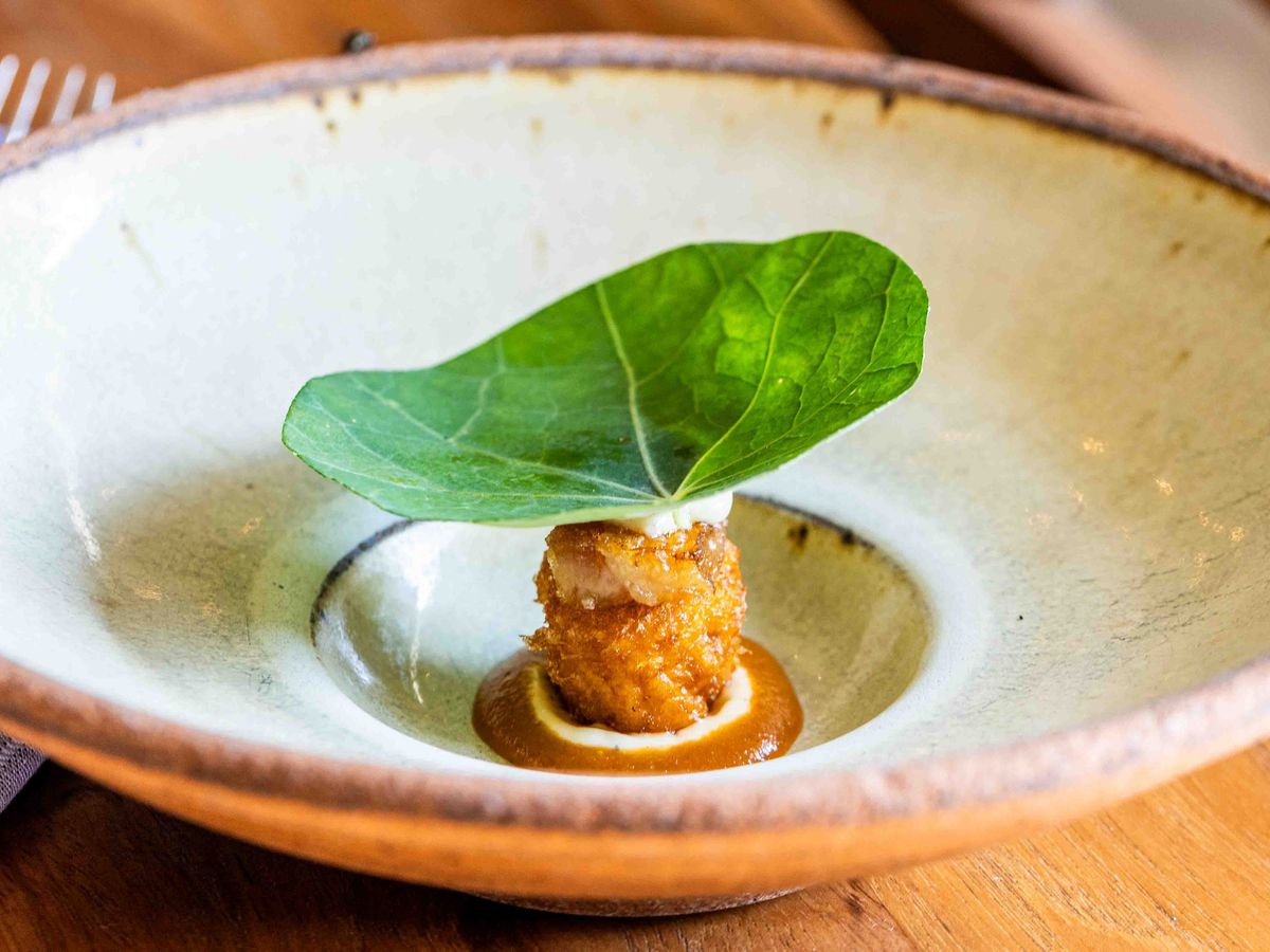 A fried shrimp topped with a giant green leaf on a plate.