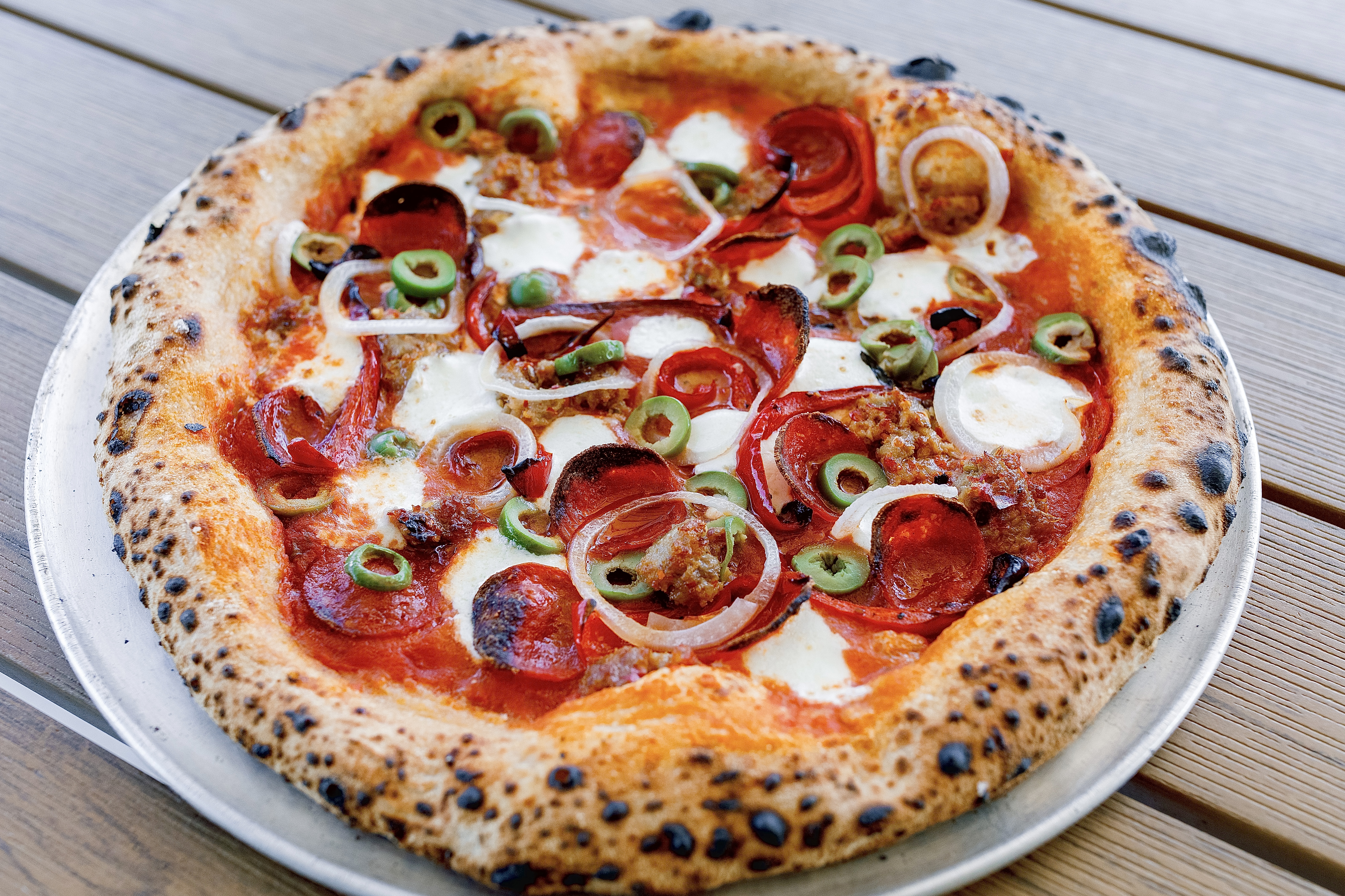 A pizza sits on a white plate. It is topped with pepperoni, olives, and onions.