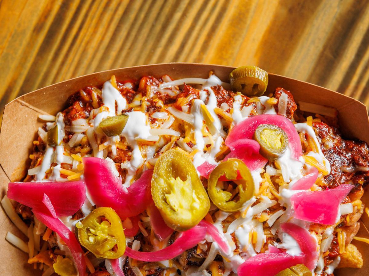 A cardboard dish of chips, chili, pickled pink onions, and sliced jalapenos.