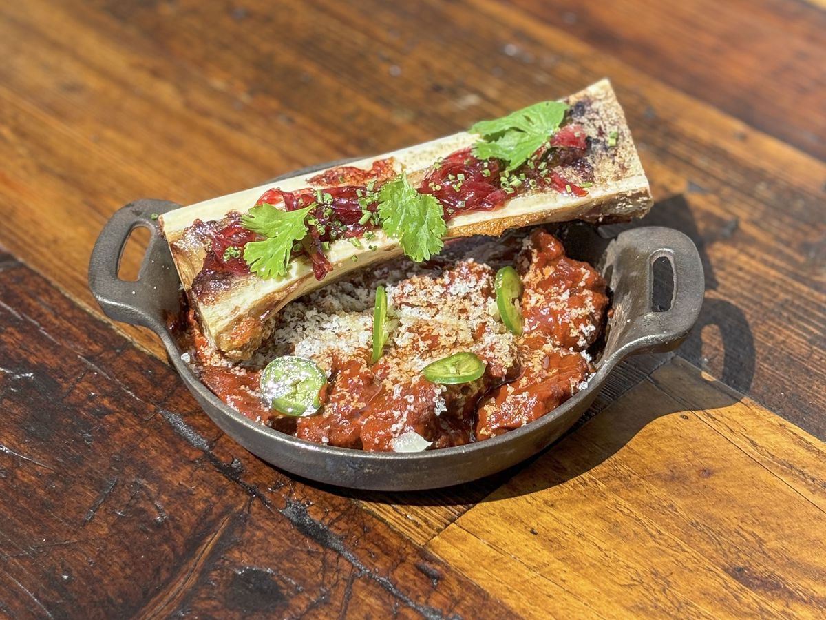 A bowl of chili in a cast iron pot with a halved bone on top of it.