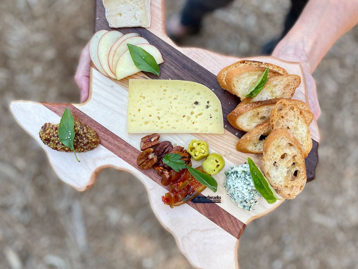 A Texas-shaped wooden board with cheeses and condiments on it.