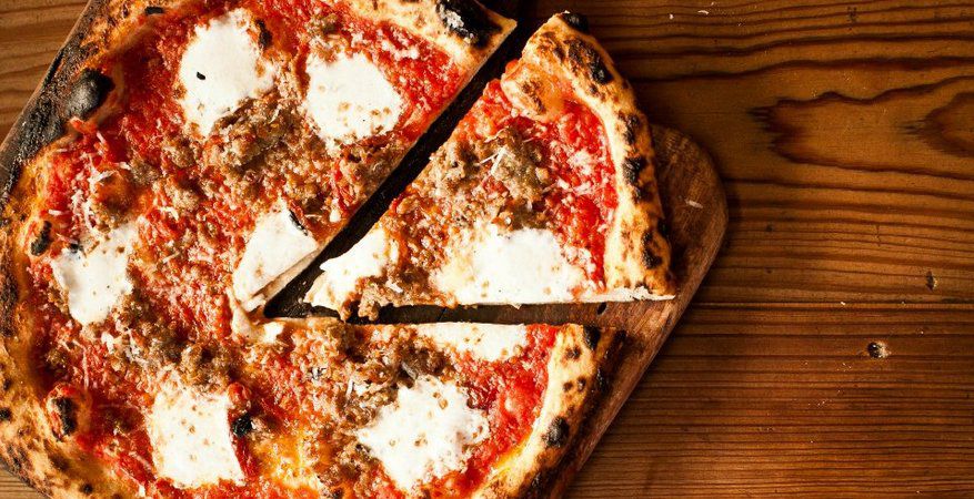 A pizza pie with red sauce, brown meat, and white cheese with a triangle-sized cut slice cut portioned out.
