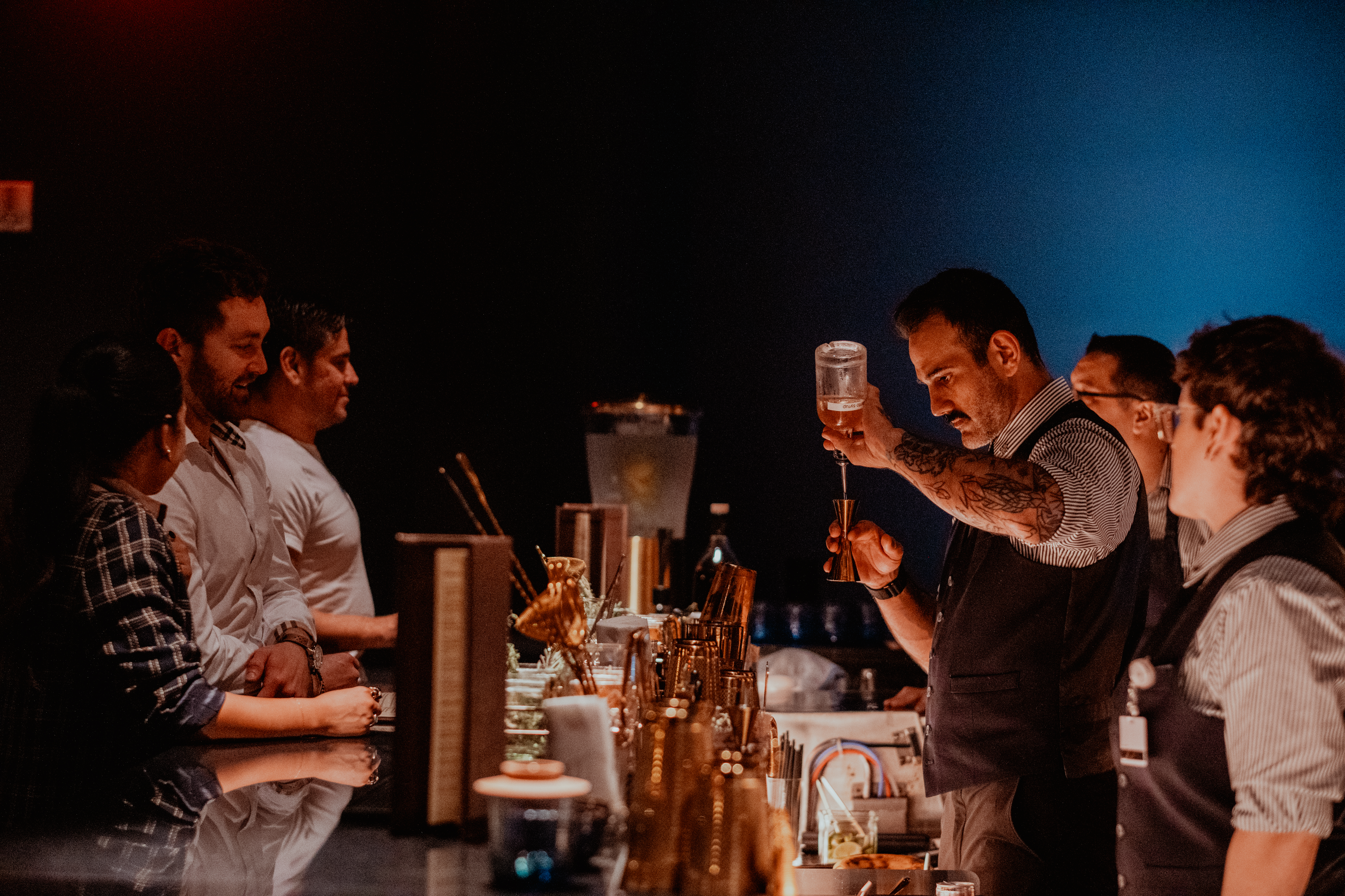 A bartender pours a cocktail while a crowd of people watch. 