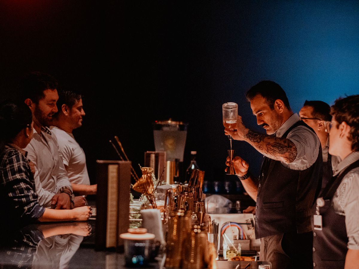 A bartender pours a cocktail while a crowd of people watch. 
