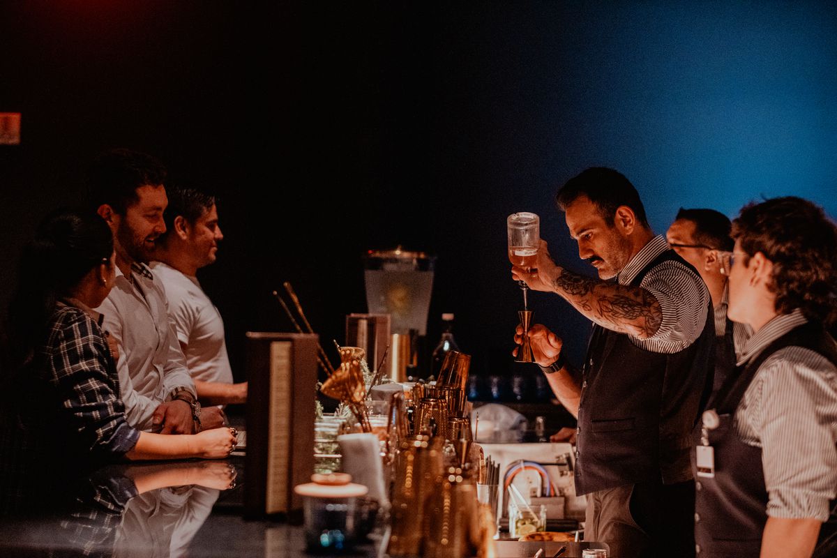A bartender pours a cocktail while a crowd of people watch. 