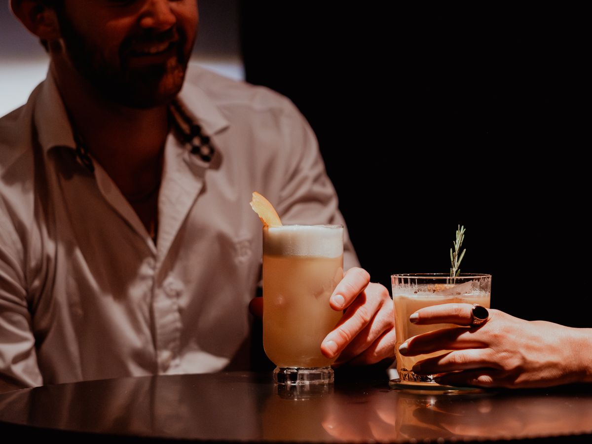 Two people sit at a bar with cocktails in front of them.