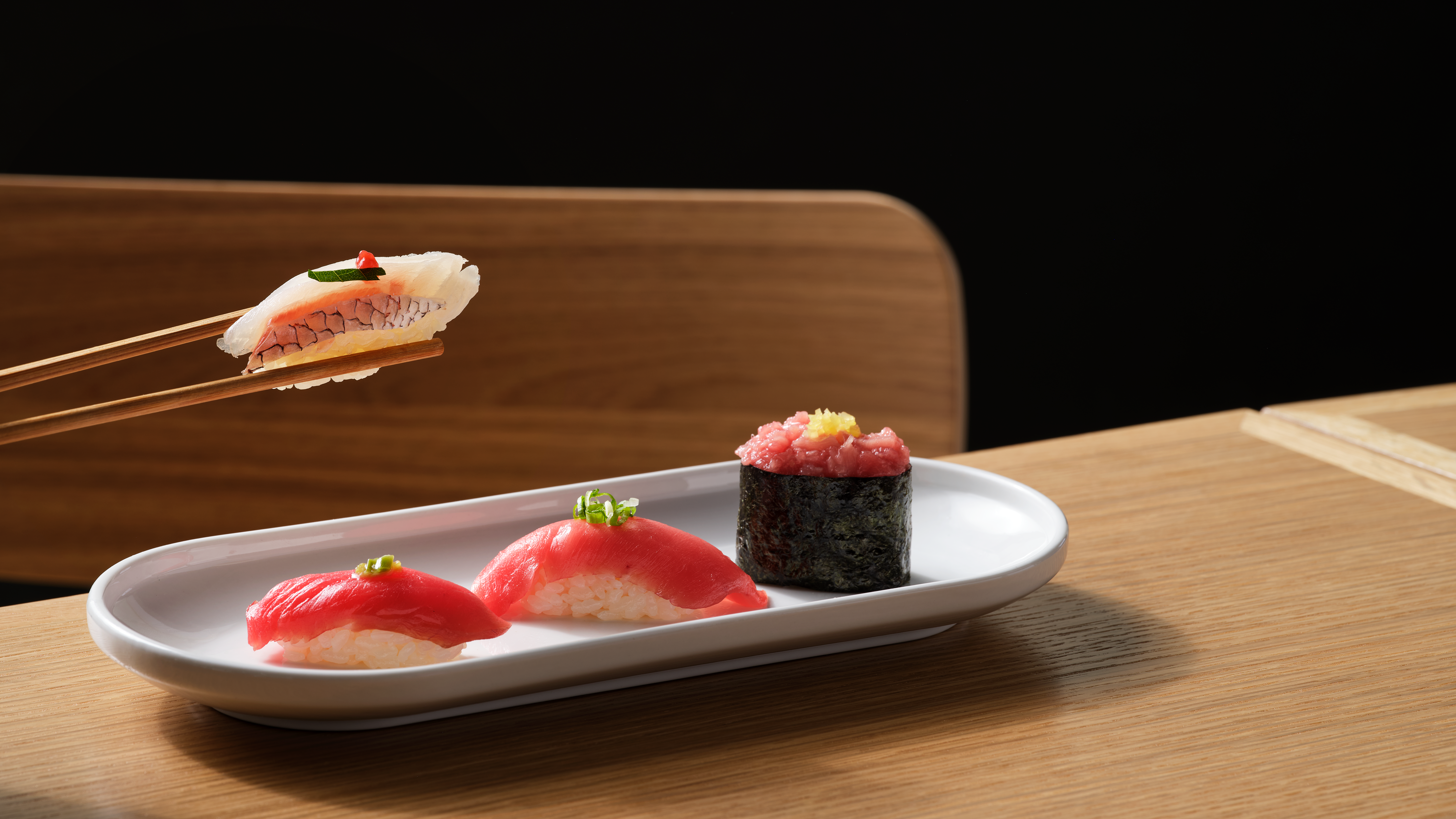 Someone picking up a sushi piece with chopsticks from a small place of three sushi.