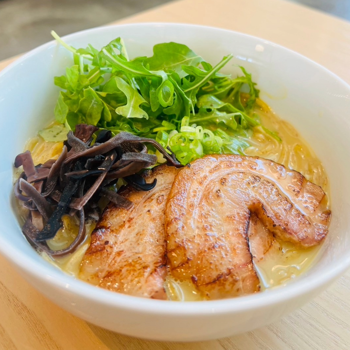 A bowl of ramen with meats, greens, and seaweed.